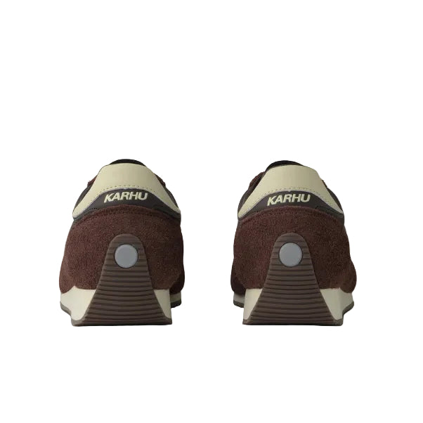A pair of KARHU slip-on shoes shown from the back, featuring a dark brown suede upper, beige heel and tongue accents, and a circular silver accent on the heel counter.