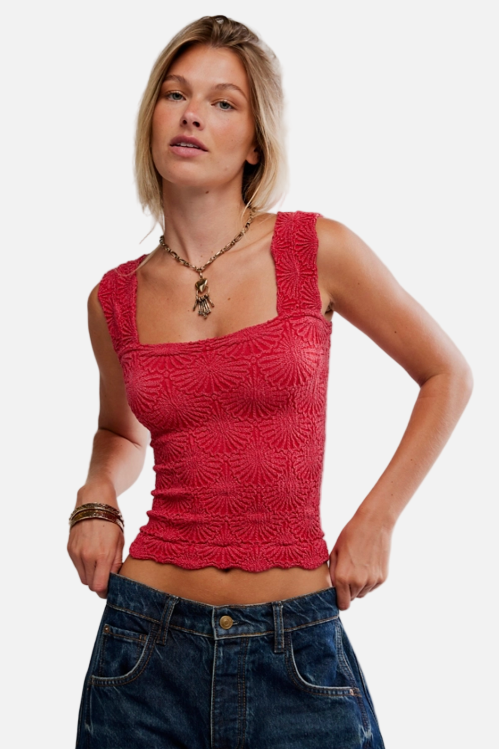 Woman wearing a red lace top and blue jeans against a plain background