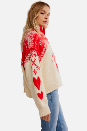 Woman wearing a red and white patterned sweater with hearts on a plain background