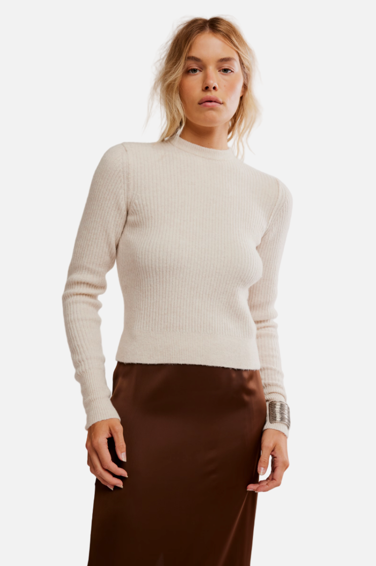 Woman wearing a beige sweater and brown skirt against a plain background
