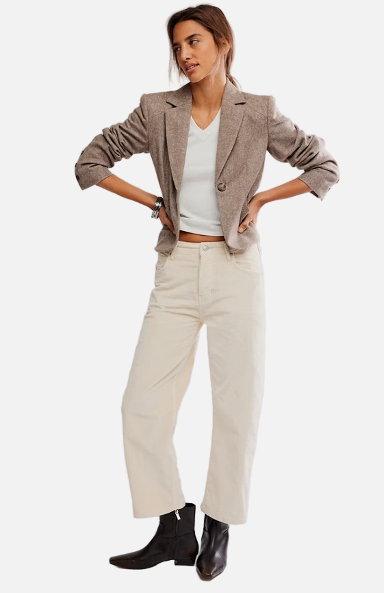 Woman wearing a beige blazer, white top, and cream pants on a plain background