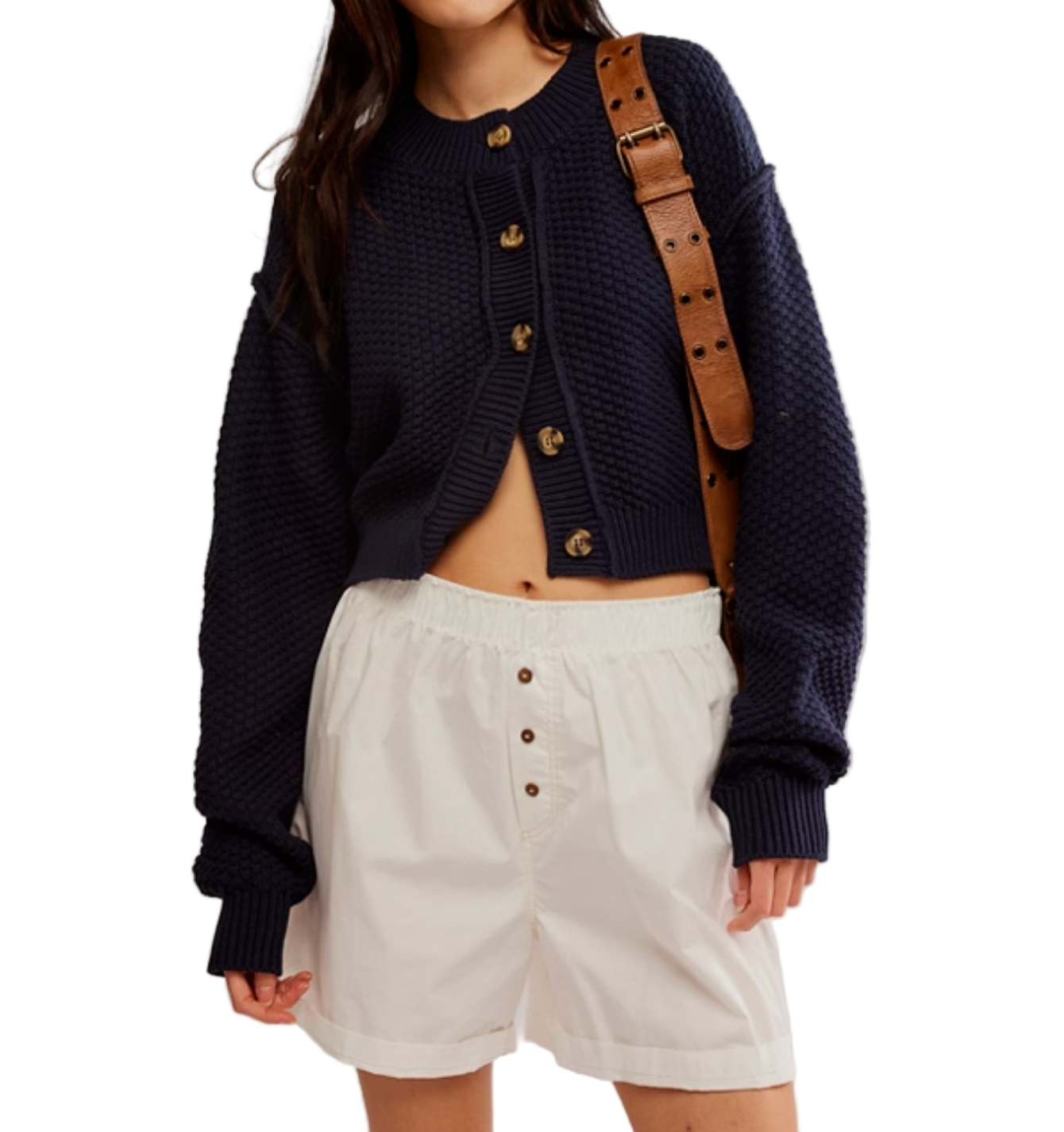 Person wearing a navy cardigan and white shorts with a brown strap over shoulder on a light gray background