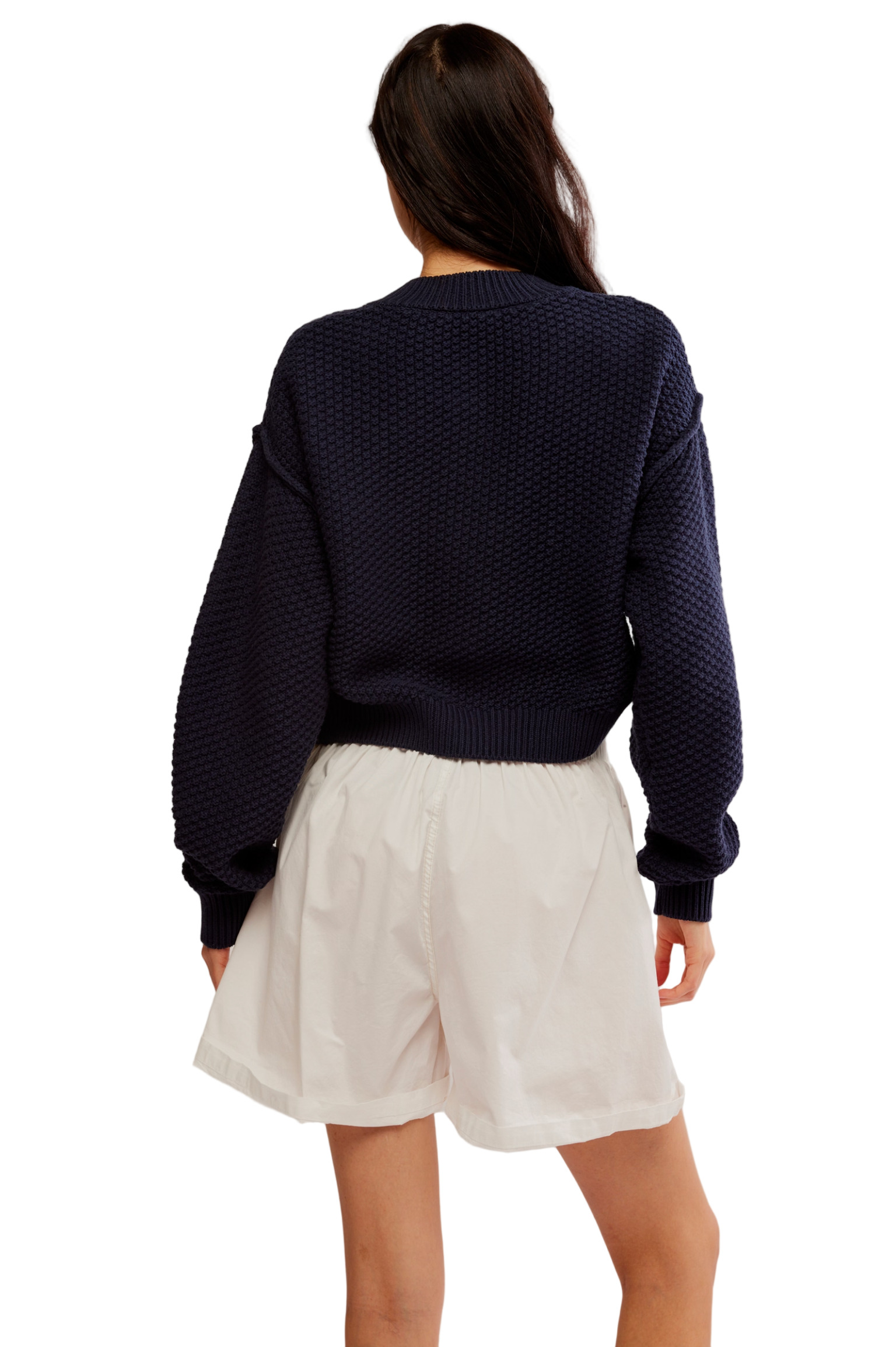Person wearing a navy sweater and white shorts on a plain background
