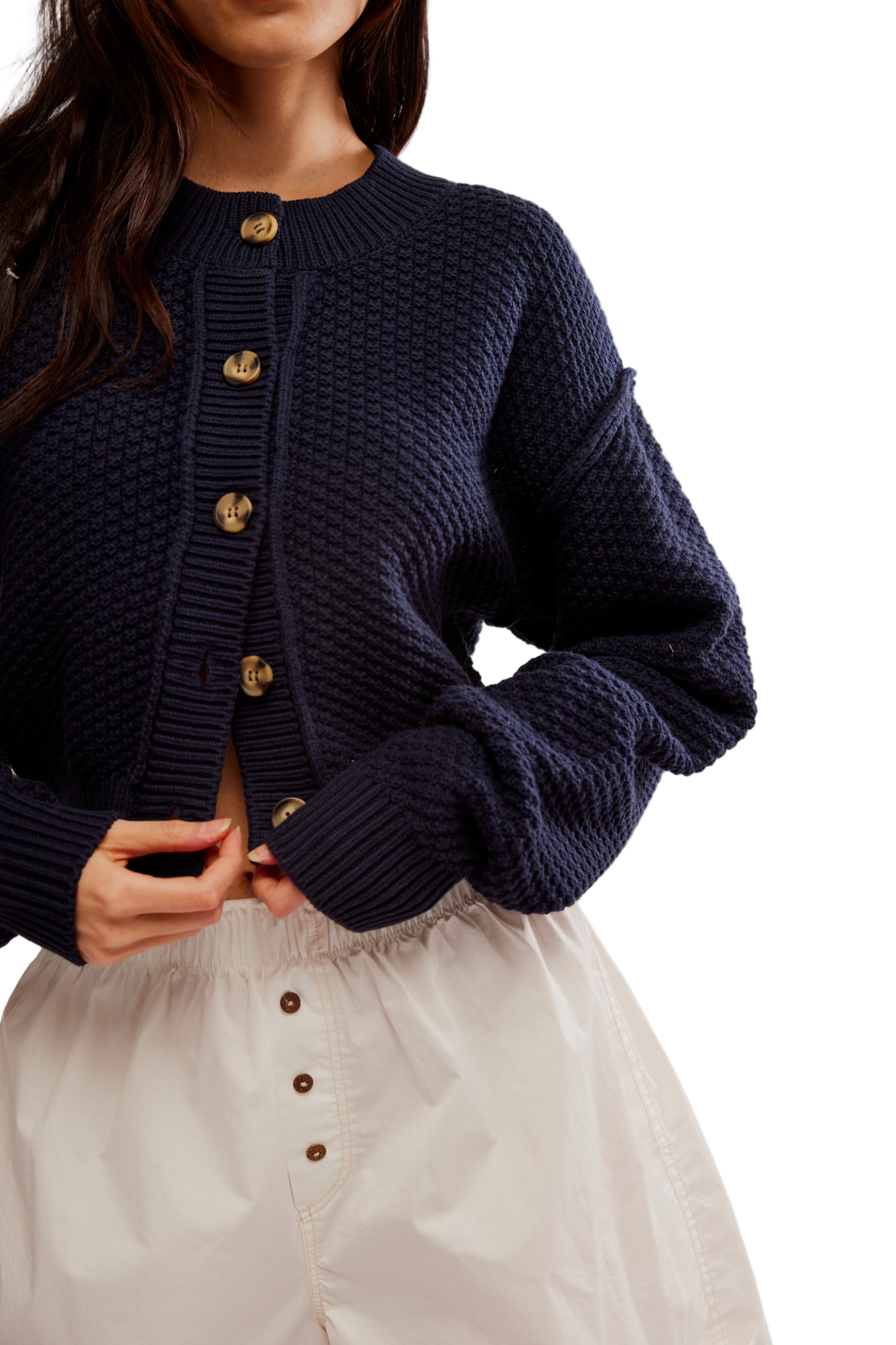 Person wearing a navy blue knitted cardigan with gold buttons on a white background