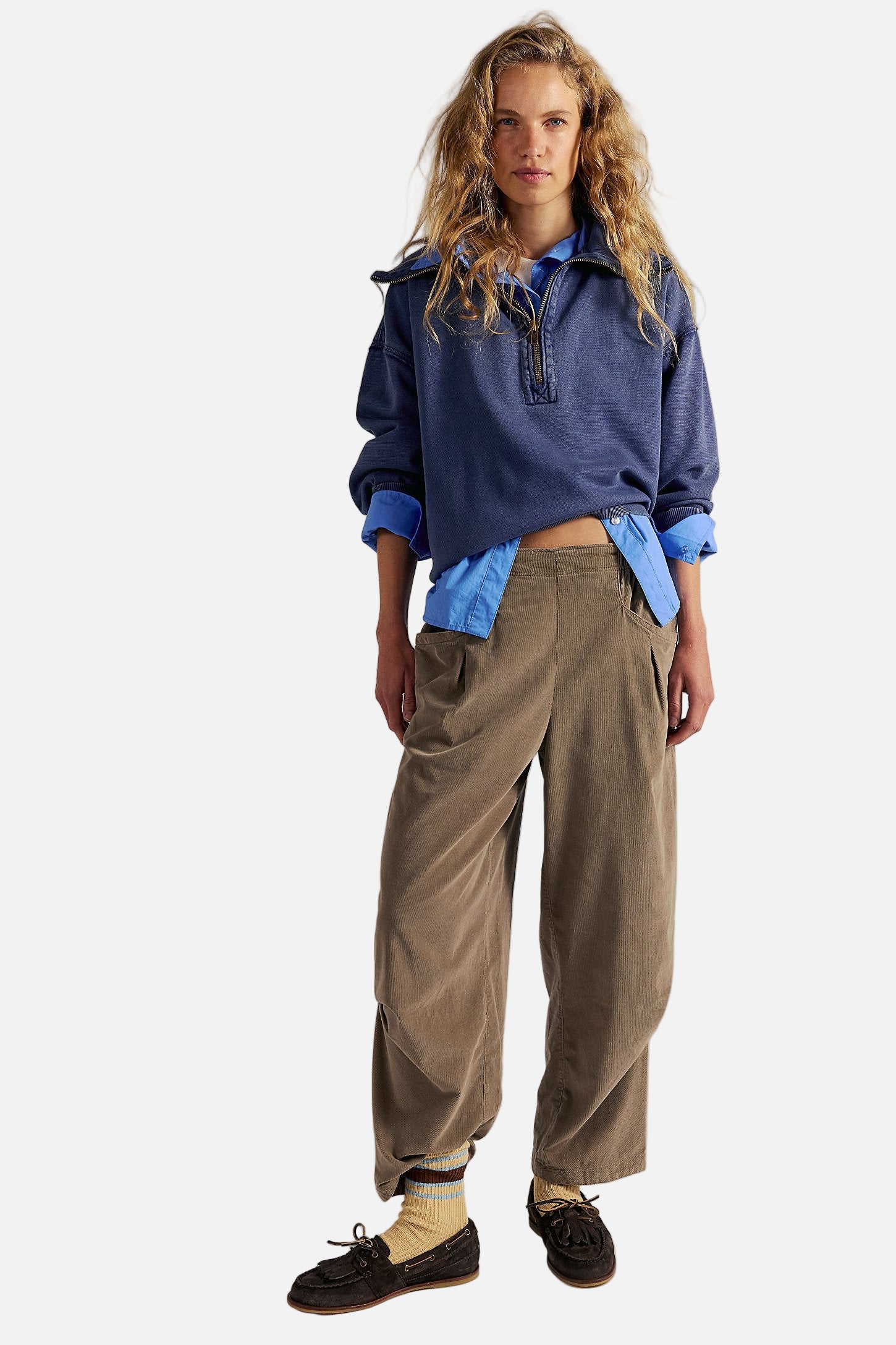 Woman wearing a blue shirt and brown pants against a plain background