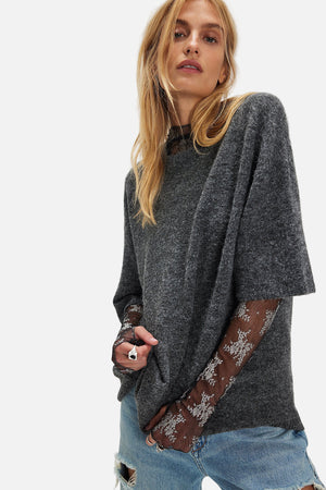 Woman wearing a dark gray poncho with lace trim on a white background
