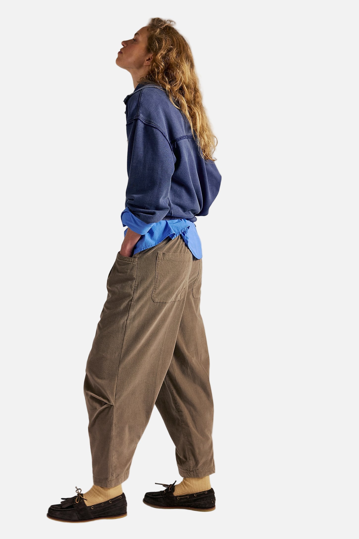 Person wearing a blue hoodie and brown pants against a plain background